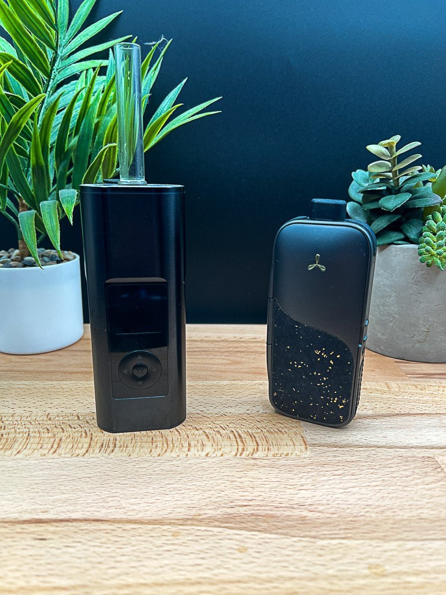 Arizer Solo 3 v2 and AirVape Legacy Pro 2 portable vaporizers side by side on a wooden surface with plants in the background.